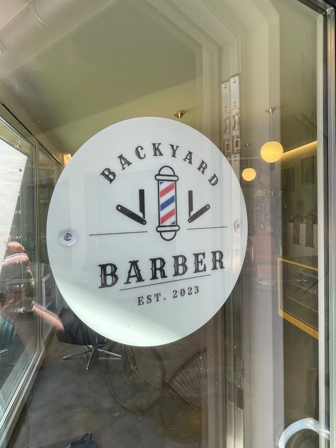 Logo Backyard Barber mit Barber-Pole und Rasiermessern auf der Schaufensterscheibe